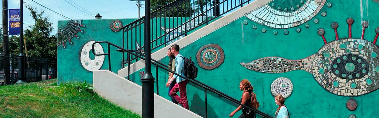 Students walking up the stairs with a mural on the wall in the background.